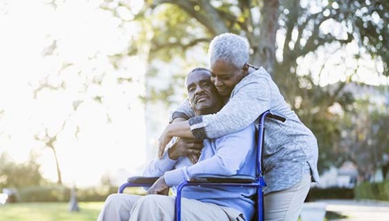 Older man in wheelchair and his caregiver hugging