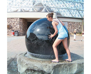 The figure shows a girl pushing on a large stone sphere.