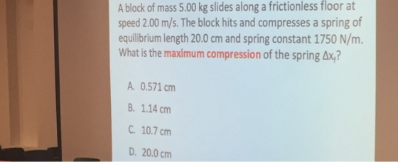 A block of mass 5.00 kg slides along a frictionless floor at speed 2.00 m/s. The block hits and compresses a spring of equili